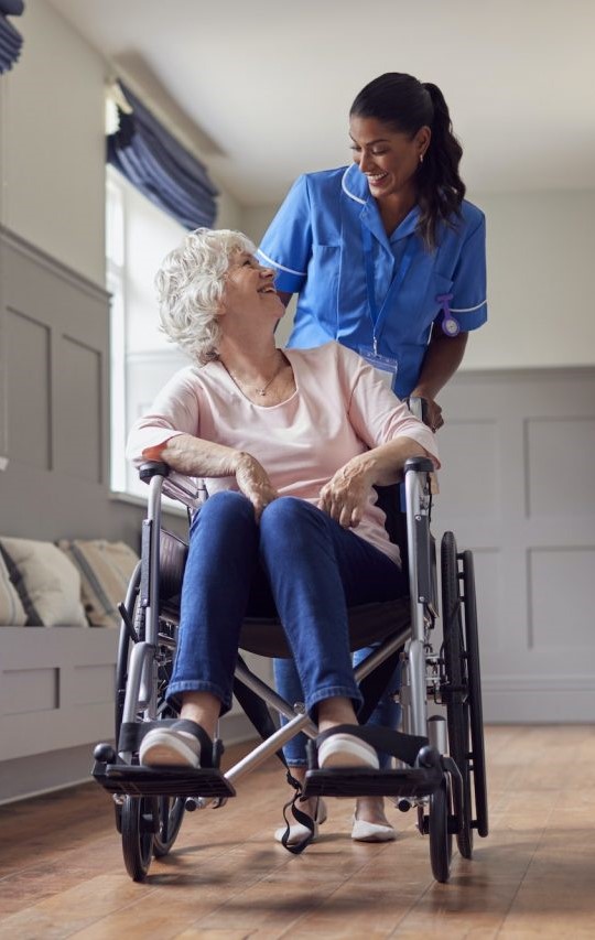 senior woman at home being pushed in wheelchair by female care worker in uniform 1